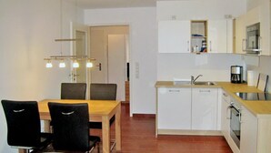 Cozinha compacta com armários brancos, mesa de jantar de madeira e cadeiras pretas, e forno embutido.