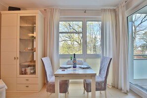 Un comedor con una mesa lista para dos, un aparador con puertas de cristal y vistas a árboles a través de amplios ventanales.