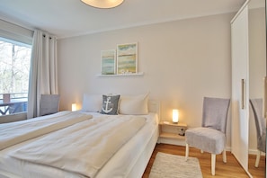 Un dormitorio con dos camas, una silla, una mesita de noche y una ventana con cortinas.