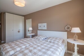 Ett sovrum med två sängar, en garderob, ett runt bord med en lampa och en spegel som hänger på väggen.