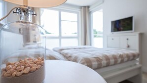 A bedroom with a bed, a bedside table with a glass jar containing seeds, and a window with curtains. - Strandglück Apartment 8A StrandGutFinder.de - Strandglück Haus A (Scharbeutz)