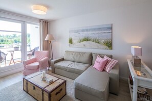 Ett vardagsrum med en soffa, en fåtölj och ett bord med en resväska på. Det finns en tavla på väggen och en lampa på ett sidobord.