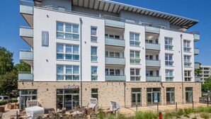 A multi-story building with balconies, a ground-level cafe, and a brick facade. - Strandglück Apartment 8A StrandGutFinder.de - Strandglück Haus A (Scharbeutz)