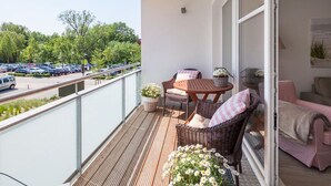 A balcony with wicker furniture, a table, and a view of a parking lot and trees. - Strandglück Apartment 8A StrandGutFinder.de - Strandglück Haus A (Scharbeutz)