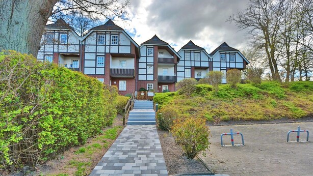 A row of traditional half-timbered houses with a paved pathway leading to the entrance.