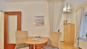 A cozy room with a round wooden table, two wicker chairs with cushions, a wooden cabinet, and a window with curtains.