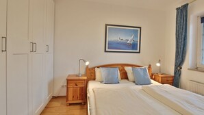 A bedroom with a large bed, wooden nightstands, a headboard with pillows, a framed picture on the wall, and a window with curtains.