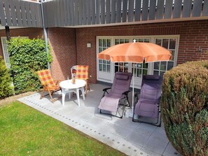 A patio with two lounge chairs, a table, and an umbrella. - Seepark Appartement 13 - Seepark (Scharbeutz)