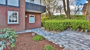 A two-story brick building with a balcony, a small front garden, and a paved walkway.