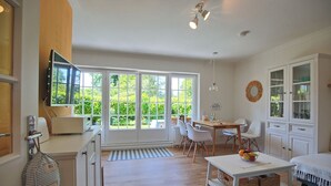 A bright, open-plan living space with a kitchen, dining area, and a large window offering a view of greenery.