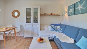 A living room with a blue sofa, white cabinet, wooden dining table, and a fruit basket.