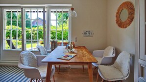 A dining room with a wooden table, white chairs, and a view of greenery outside.