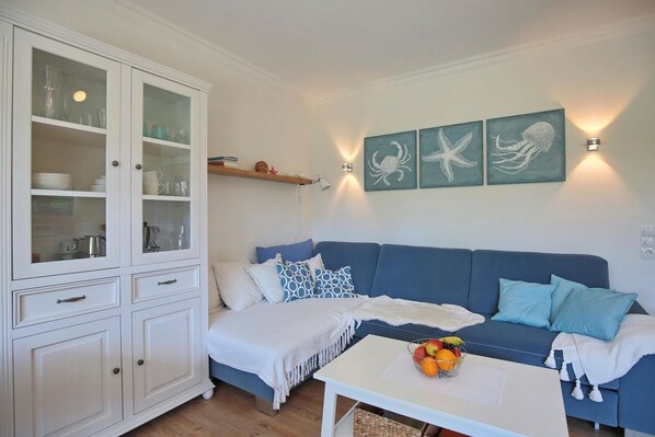 Ein Wohnzimmer mit blauem Sofa, weißem Schrank und Wandbildern von Meeresbewohnern.