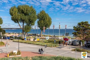 Une route côtière avec une plage en arrière-plan, un chemin piétonnier et quelques véhicules.