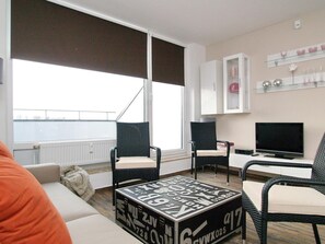 Een moderne woonkamer met een bank, twee fauteuils, een salontafel, een televisie en een kast met decoratieve objecten.