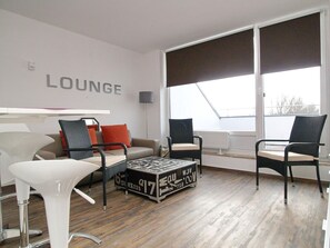 Un salon moderne comprenant un canapé, deux fauteuils, une table basse et une grande fenêtre donnant sur un paysage.