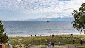 Une zone côtière comprenant un terrain de golf, une étendue d’eau et un voilier visible au loin.