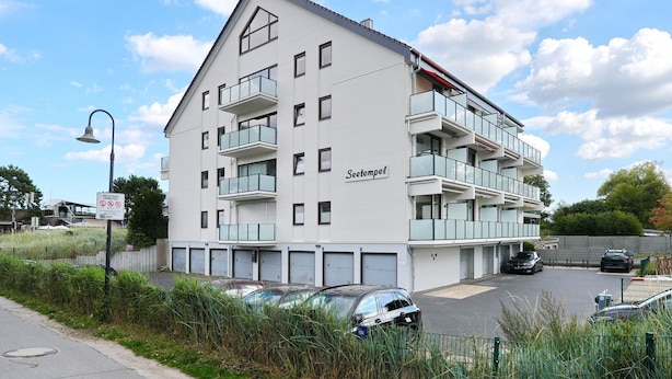 Un immeuble à plusieurs étages doté de balcons, une enseigne indiquant « Seetempel », et plusieurs voitures garées devant.