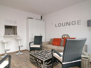 Een moderne zithoek met een bank, twee rieten fauteuils, een klein tafeltje en een kast.