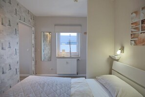Een slaapkamer met een bed, een raam met zonwering, een radiator en een wandplank met een lamp.
