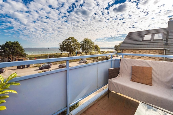A balcony with a view of the sea, a covered outdoor seating area, and a building with a sloped roof.