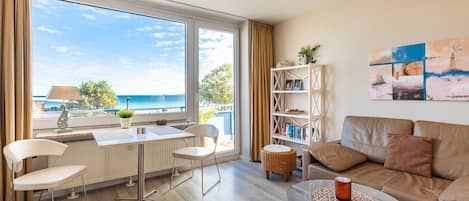Una sala de estar moderna con vistas al mar, un comedor con mesa y sillas, una estantería y un sofá.