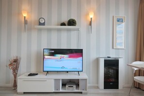 A modern living room with a flat-screen TV on a white entertainment unit, a fireplace, and a striped wall.
