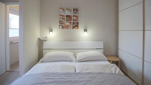 Een slaapkamer met een bed, twee nachtkastjes, een wandplank met decoratieve objecten en een raam.