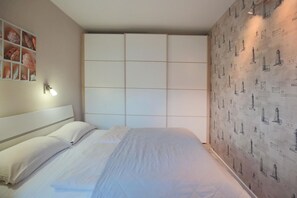 A bedroom with a bed, a headboard, a wall with a light fixture, and a patterned wallpaper.