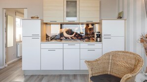Een moderne keuken met witte kastjes, een rieten stoel en een koffieapparaat.