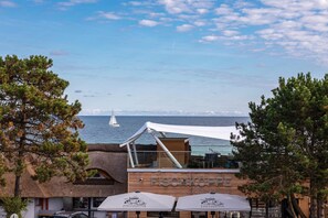 A coastal restaurant with a view of the sea, featuring a wooden facade and outdoor seating with umbrellas. - Seetempel Apartment 39 - Seetempel (Scharbeutz)
