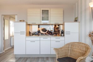 Een moderne keuken met witte kastjes, een rieten stoel en een koffieapparaat.