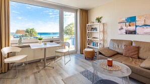 Een moderne woonkamer met uitzicht op zee, een eethoek met tafel en stoelen, een boekenkast en een bank.