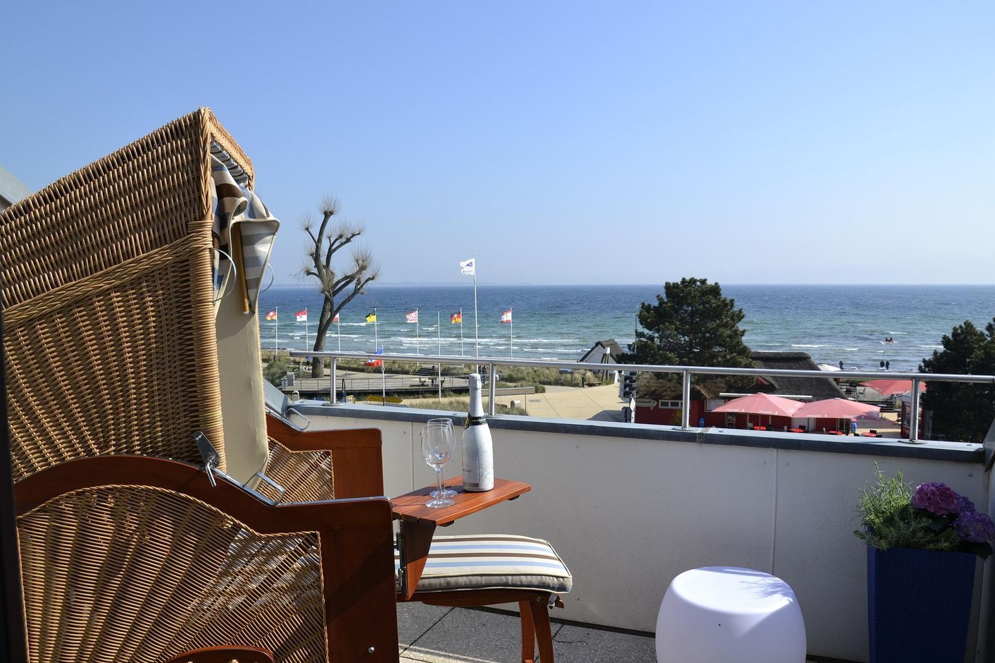Een rieten stoel en tafeltje met een fles en glas op een balkon met uitzicht op het strand.