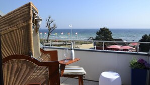Een rieten stoel en tafeltje met een fles en glas op een balkon met uitzicht op het strand.