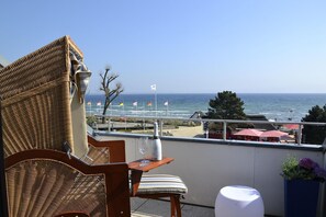 A wicker chair and table with a bottle and glass on a balcony overlooking the beach. - Seetempel Apartment 45 - Seetempel (Scharbeutz)