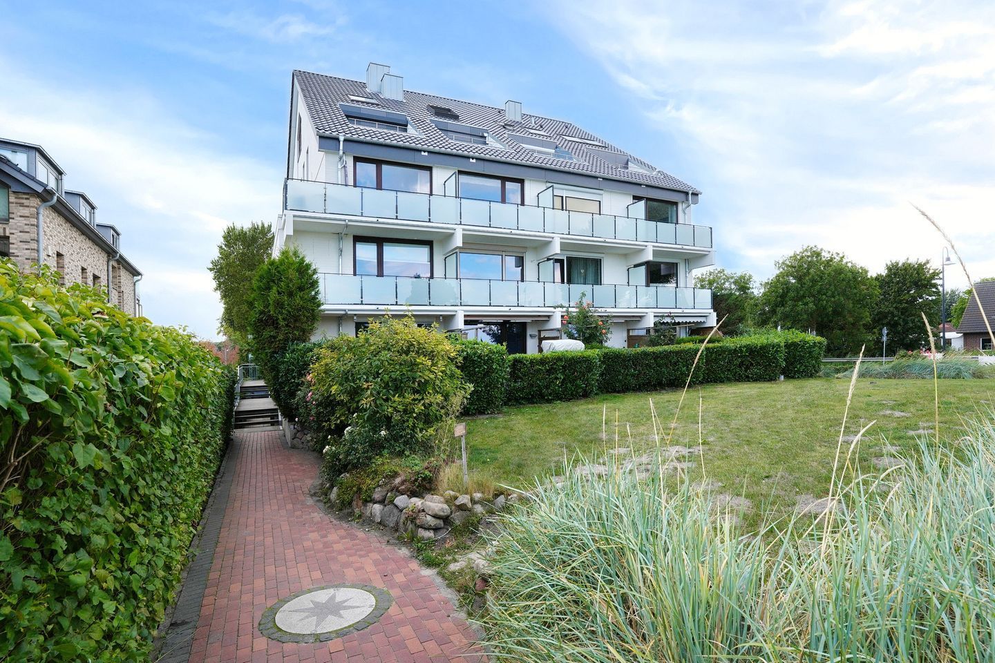 A multi-story residential building with a brick facade, a paved pathway, and a well-maintained garden.