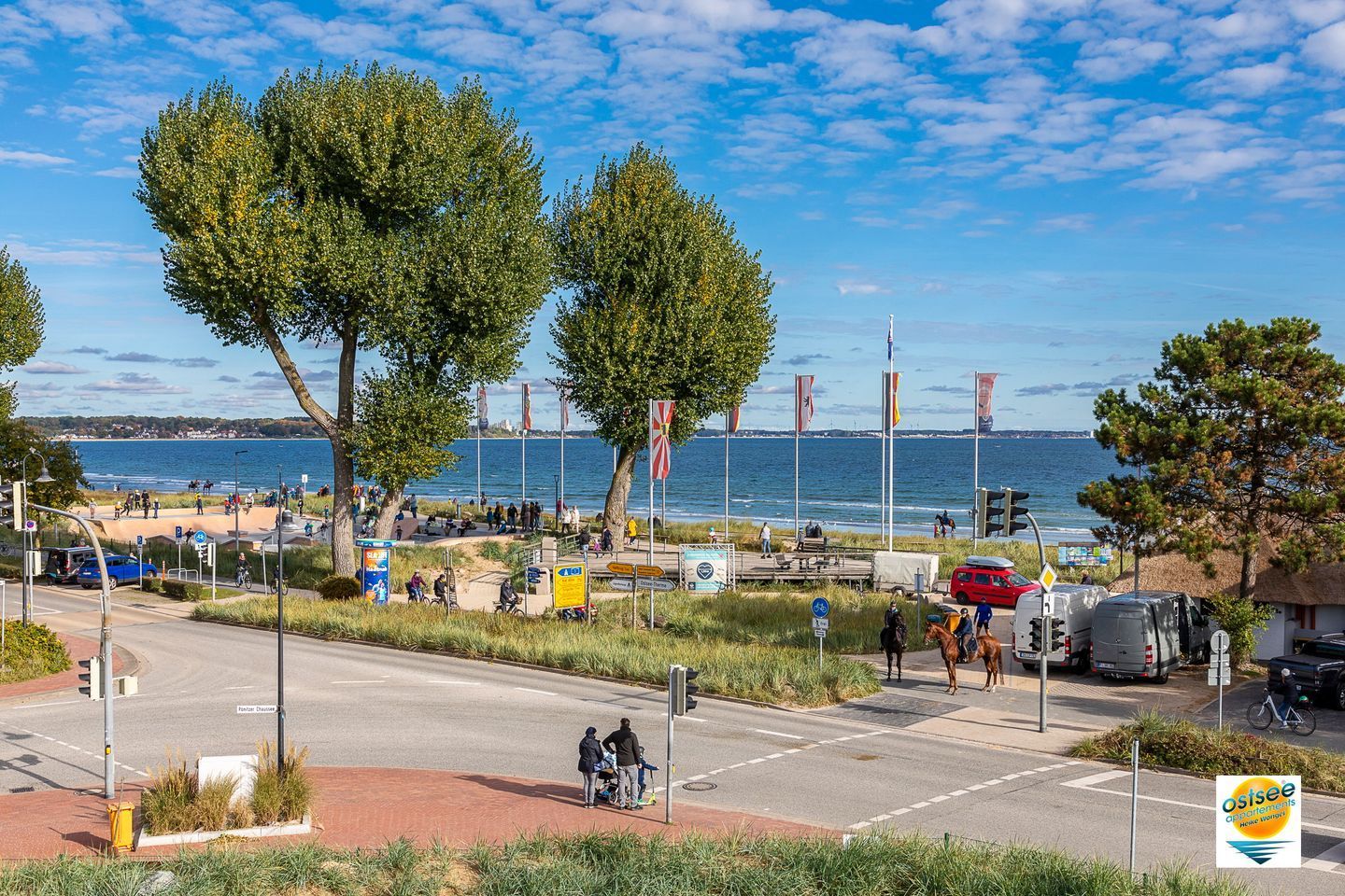 A coastal road with a beach in the background, a pedestrian path, and a few vehicles.