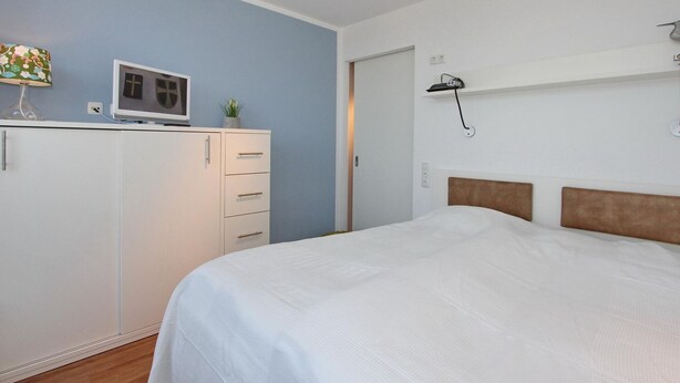 Een slaapkamer met een bed, een kledingkast, een bureau met lamp en een tv aan de muur.