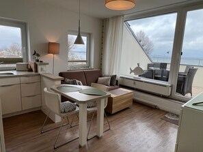 A modern kitchen with a dining area, a sofa, and a view of the sea. - Seetempel Apartment 45 - Seetempel (Scharbeutz)
