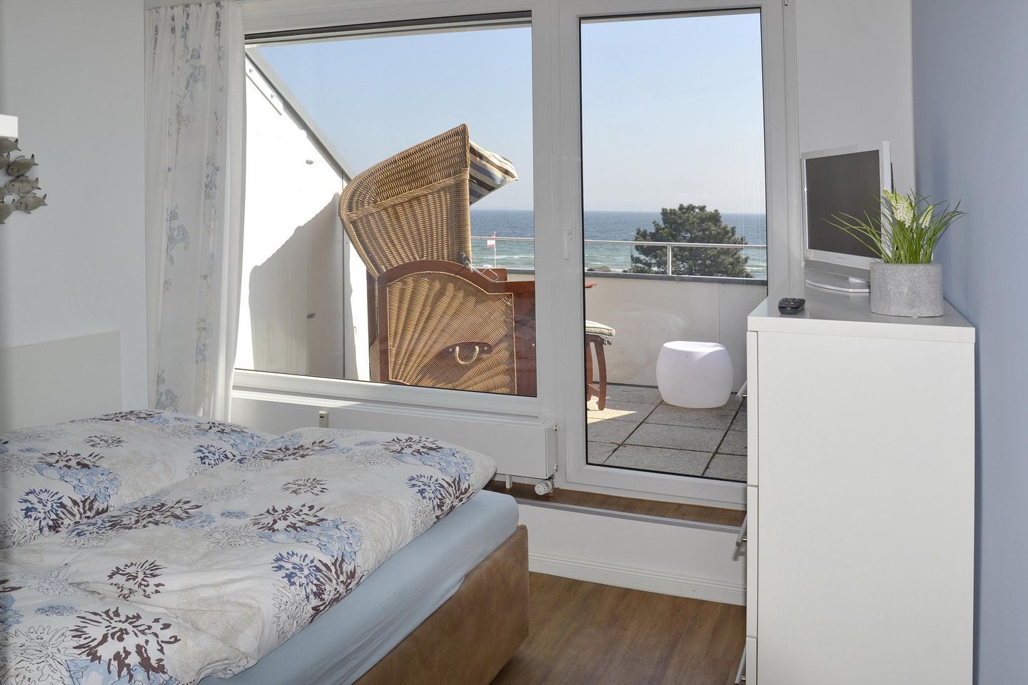Une chambre avec un lit, une fenêtre, un balcon et une petite table sur laquelle est posée une plante.
