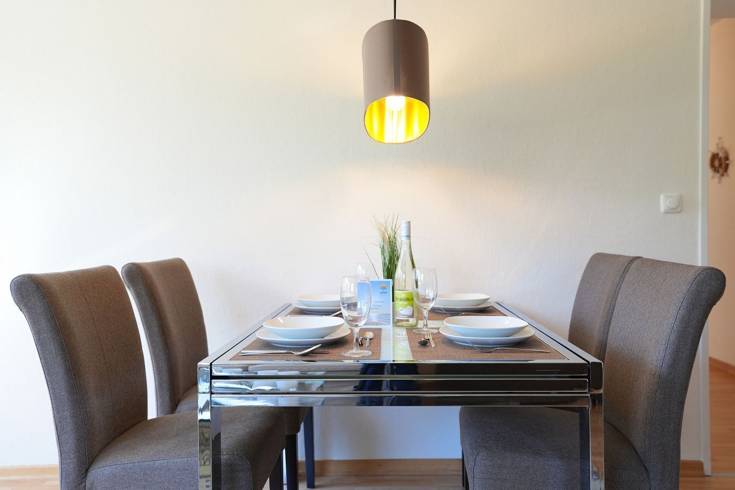 A dining table with four chairs, a hanging light fixture, and a bottle of wine on the table.