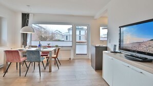A modern kitchen with a dining area, large windows, and a flat-screen TV.