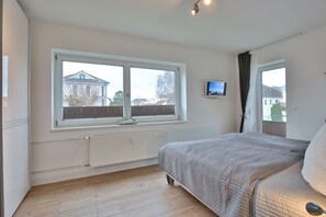 A bedroom with a bed, a window with blinds, a mounted TV, and a radiator.