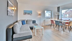 A modern living room with a grey sofa, a small coffee table, and a dining area with a table and chairs.