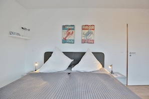 Une chambre à coucher moderne avec un lit, deux oreillers, une table de chevet, une lampe et deux affiches au mur.