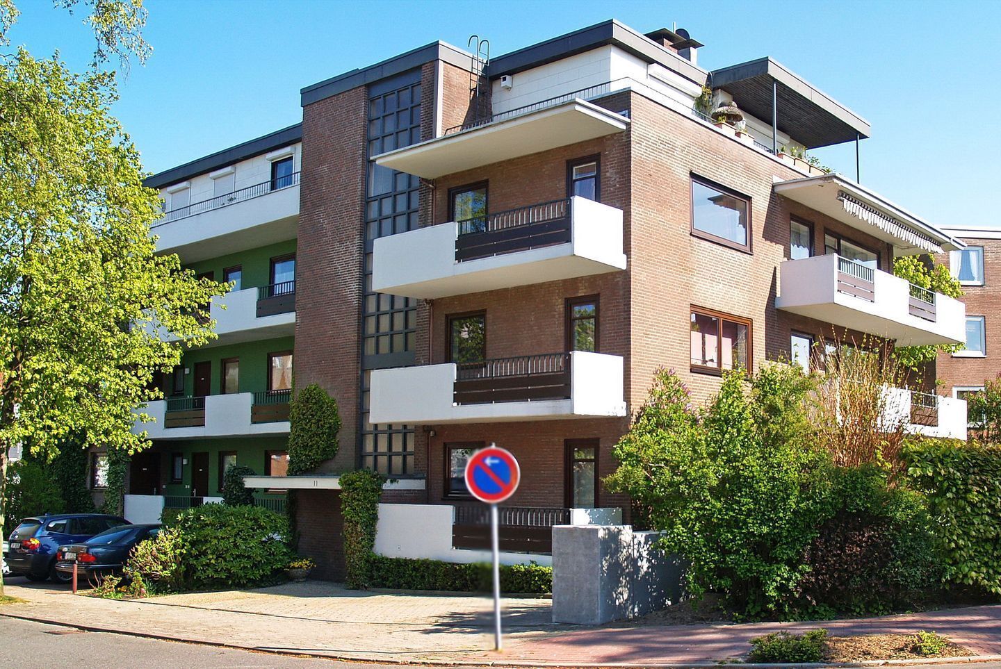 A multi-story residential building with balconies, a no parking sign, and a clear sky.