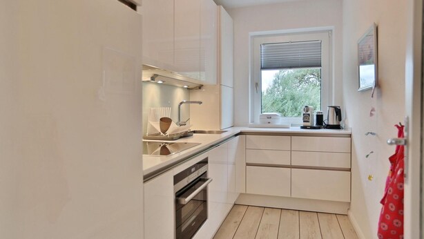Una cocina compacta con armarios blancos, un ventanal y piso de madera.