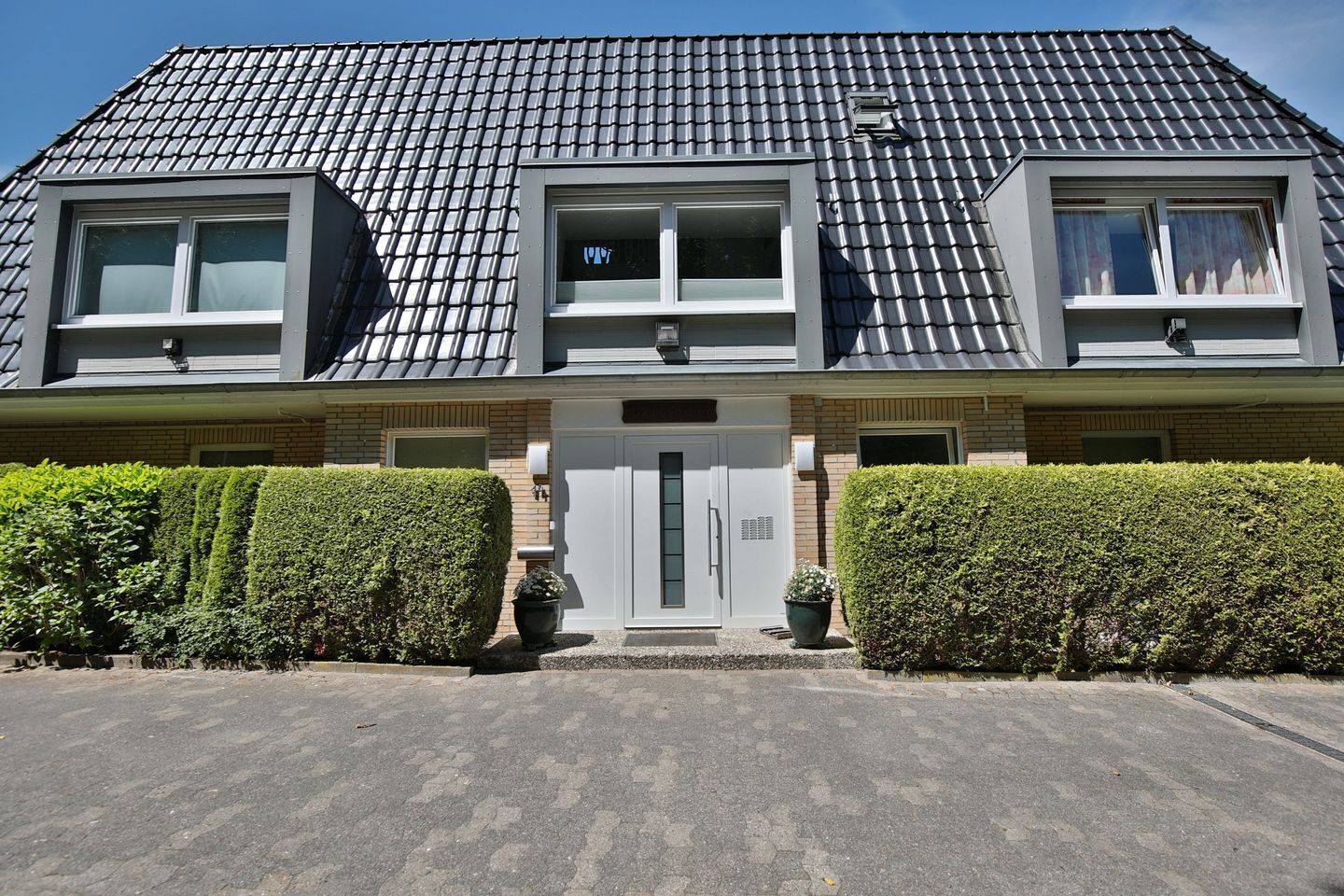 En moderne boligbygning med to etager, tag med grå fliser, en central indgangsdør og to vinduer på øverste etage.