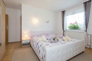 Une chambre à coucher comprenant un lit, une table de chevet, une lampe, une fenêtre avec des rideaux et une vue sur la verdure à l’extérieur.